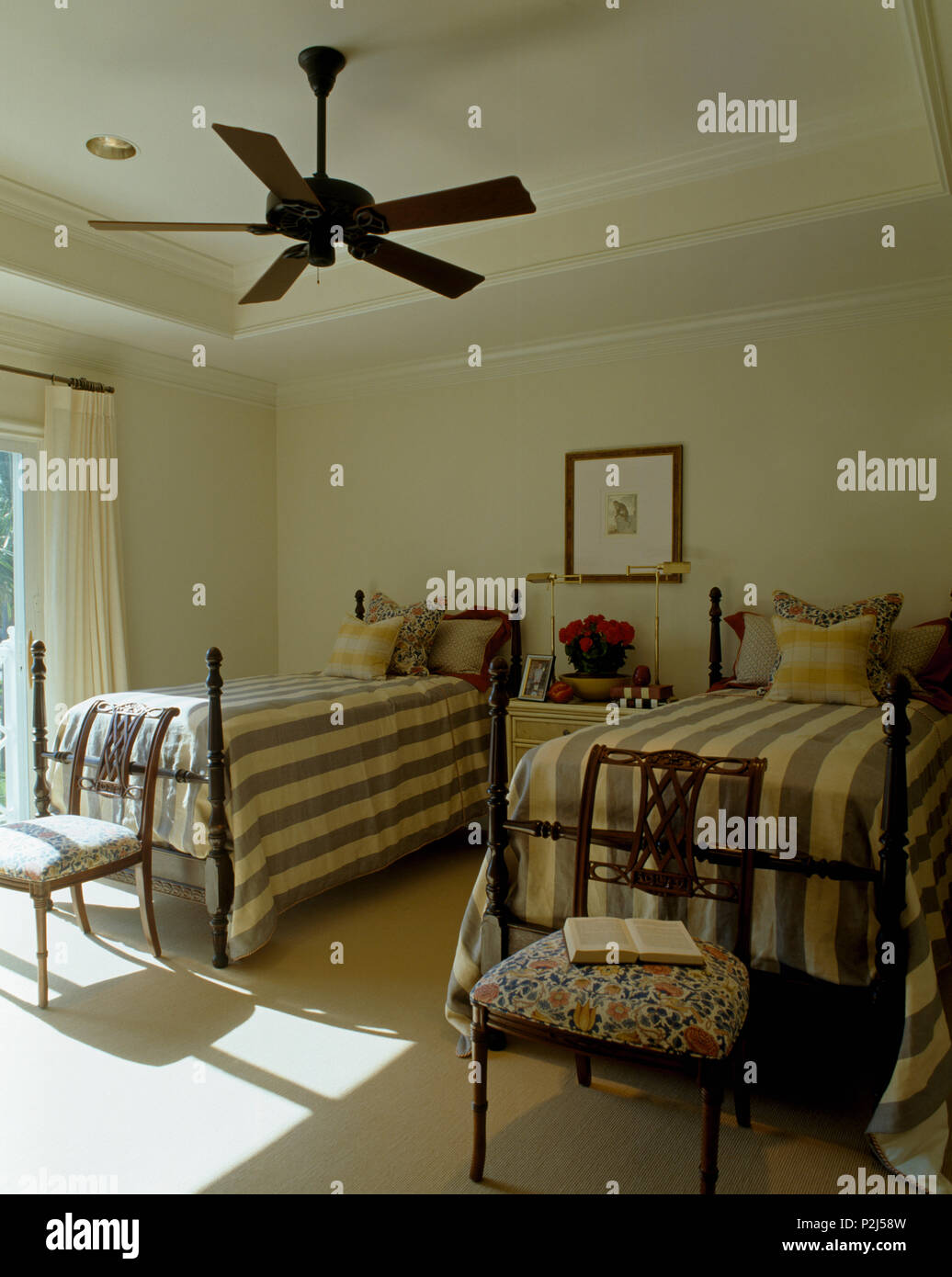Electric ceiling fan above twin beds with turned spindles and wide-striped bed-covers in coastal bedroom Stock Photo