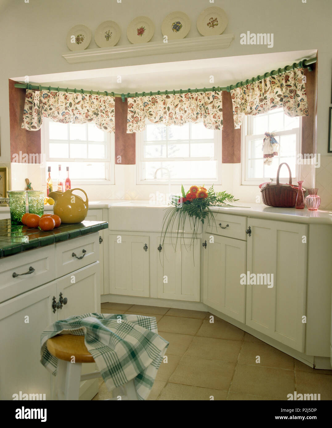 Floral pelmets on windows above sink in traditional white kitchen Stock Photo