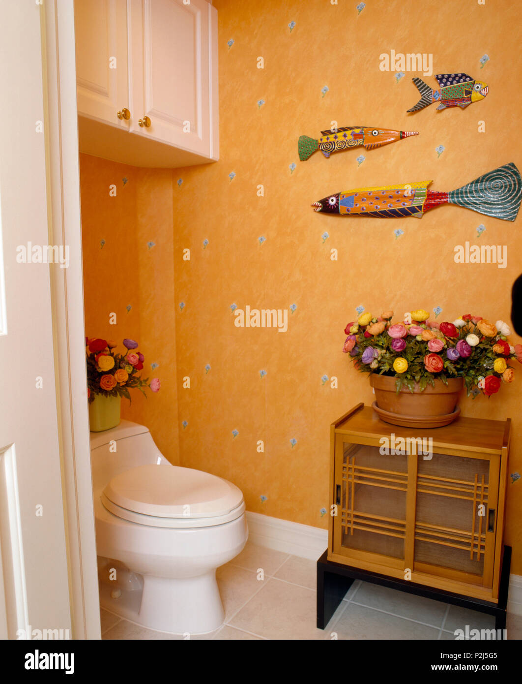 Brightly coloured wooden fishes on wall above toilet in cloakroom with orange wallpaper Stock Photo