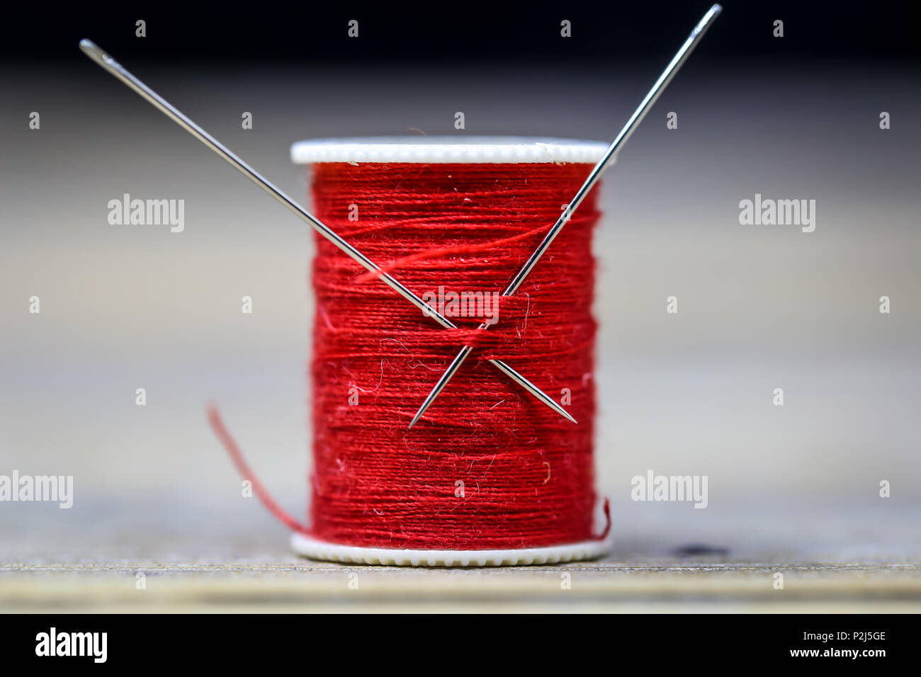 Sewing thread red with two needles closeup on wooden background Stock Photo