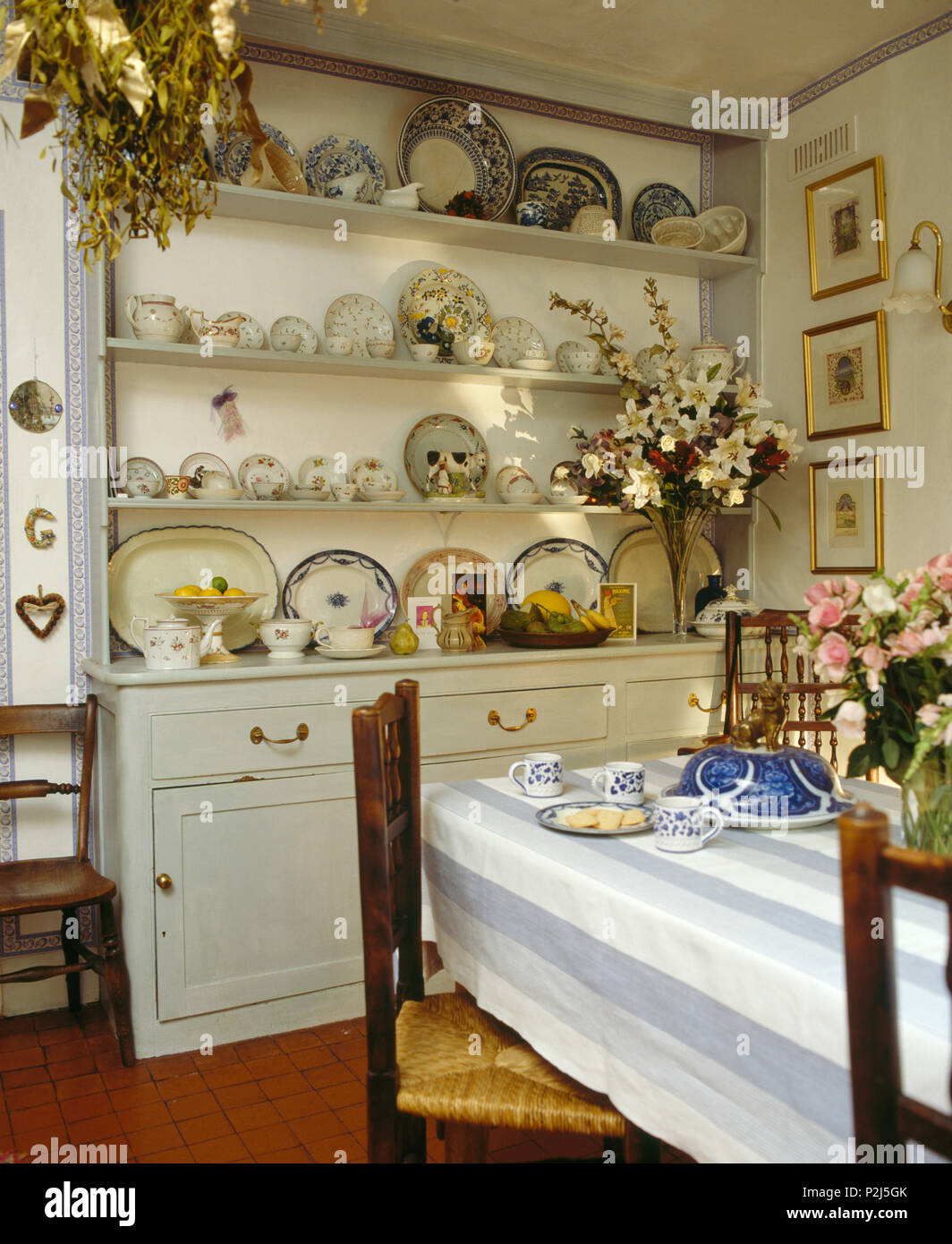 Pale grey painted fitted dresser with antique china in country dining room  with blue striped cloth on the table Stock Photo - Alamy