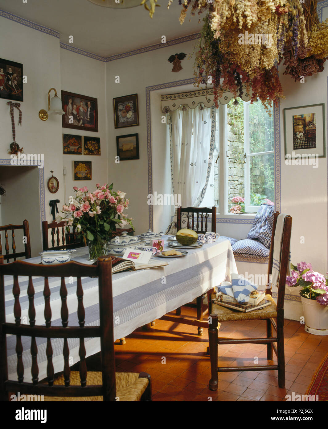 Antique rush seated chairs at table with blue striped cloth in country dining room with quarry tiled floor Stock Photo