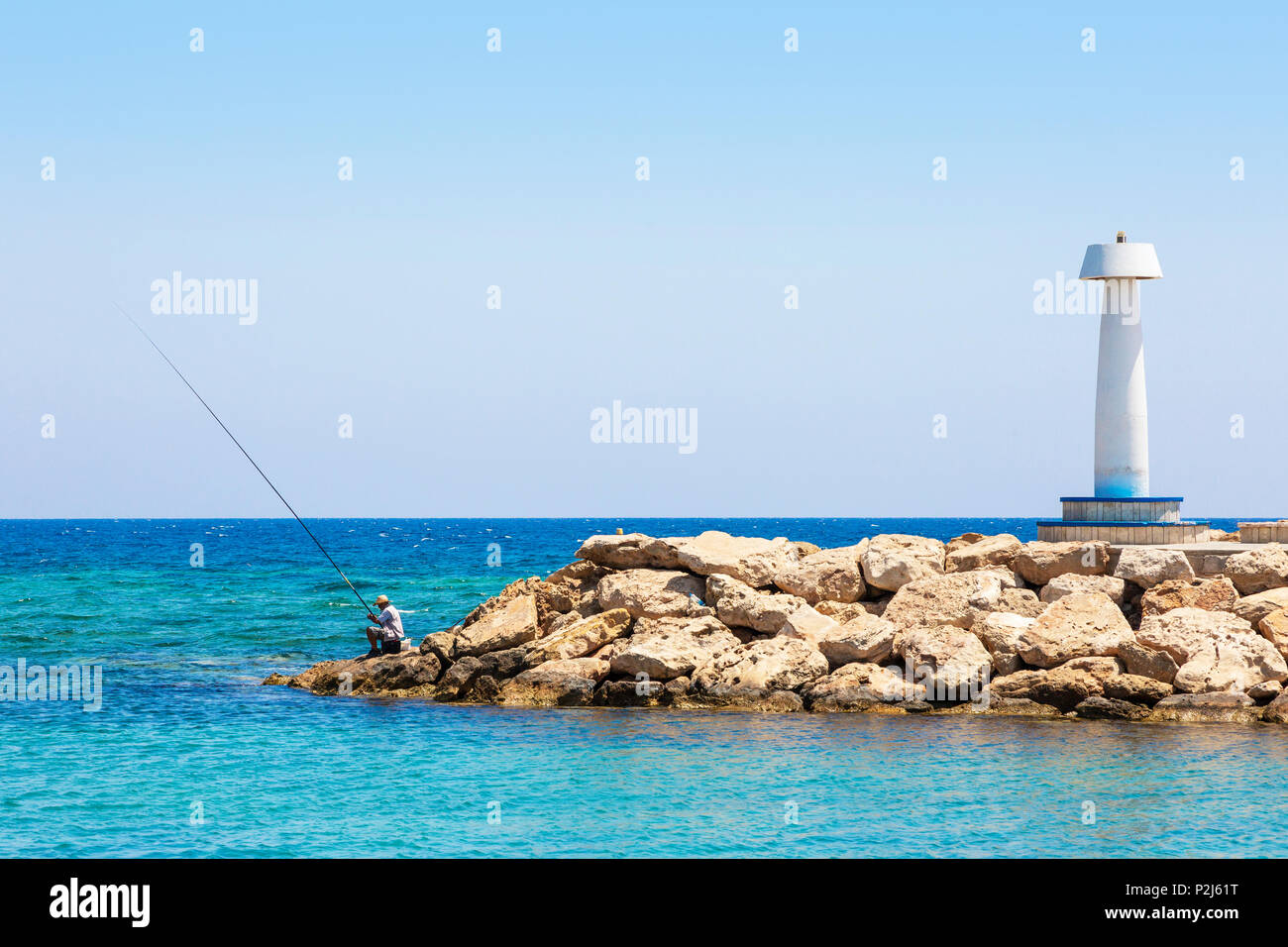 Local man fishing off the end of the marina pier at Agia Napa, Cyprus Stock Photo