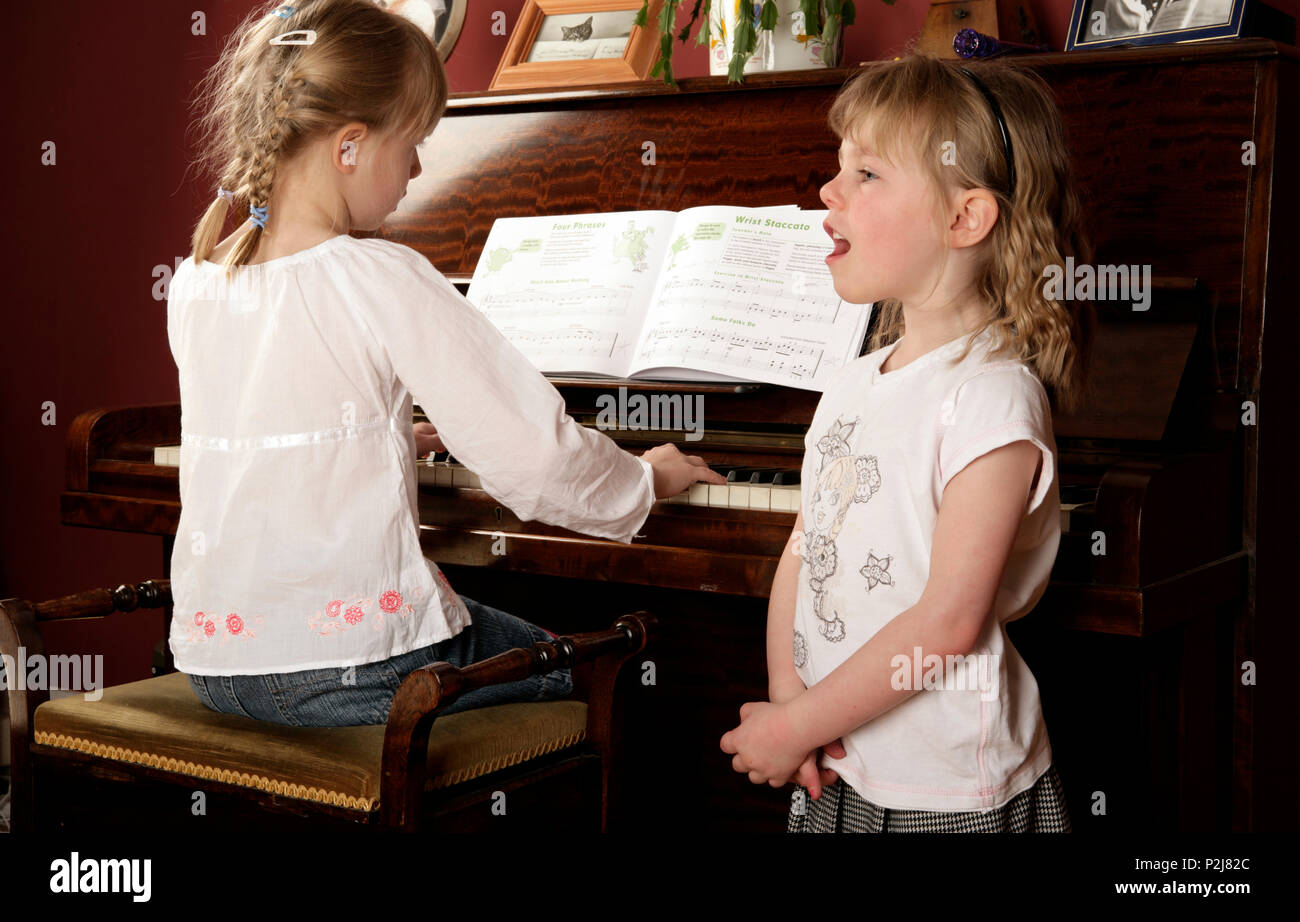 Two girls enjoying making music. One playing the piano and the other singing a song Stock Photo