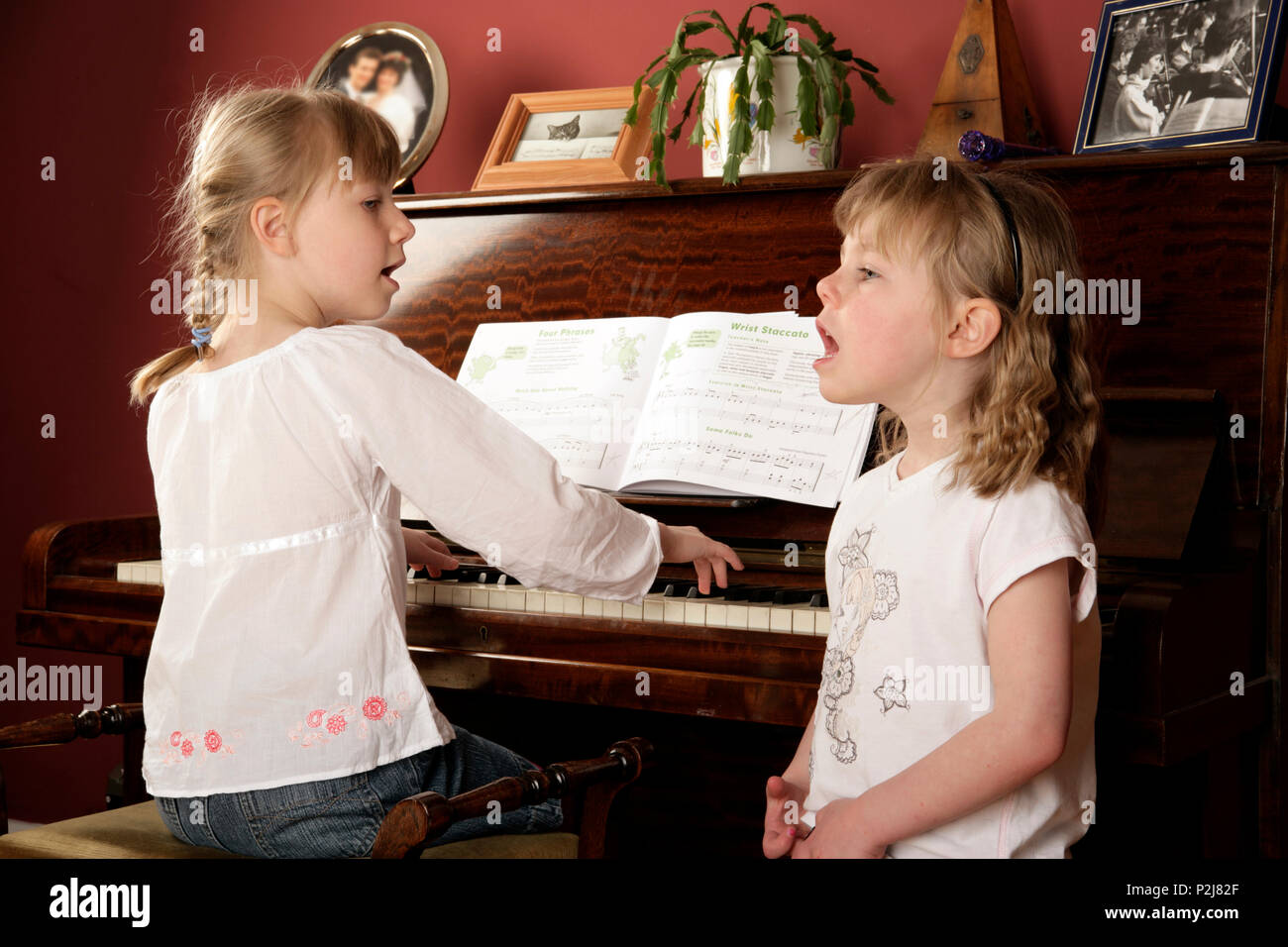 Two young girls singing whilst one also plays the piano. Room setting. Stock Photo