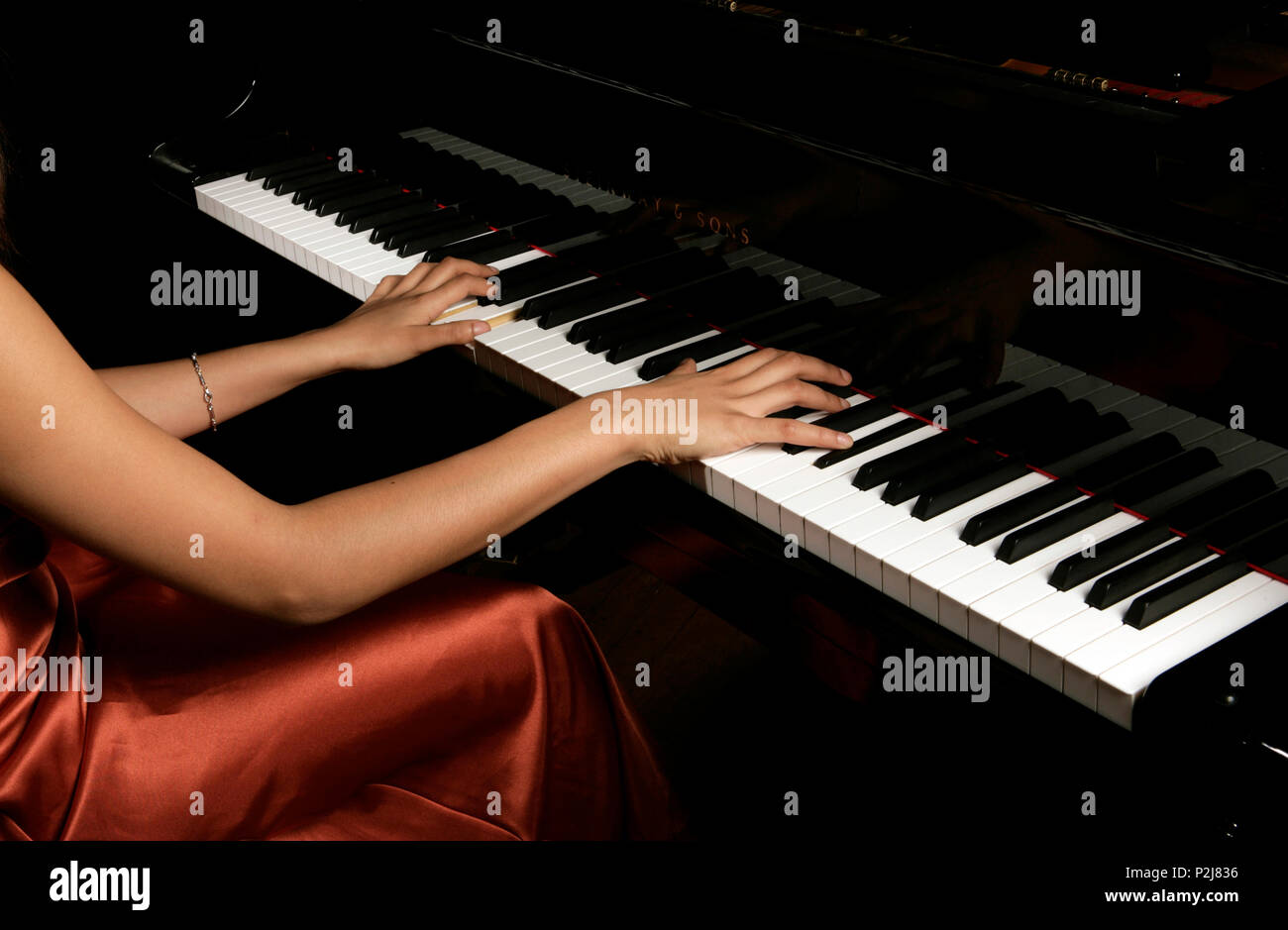 young woman playing the grand piano in a golden concert dress Stock Photo