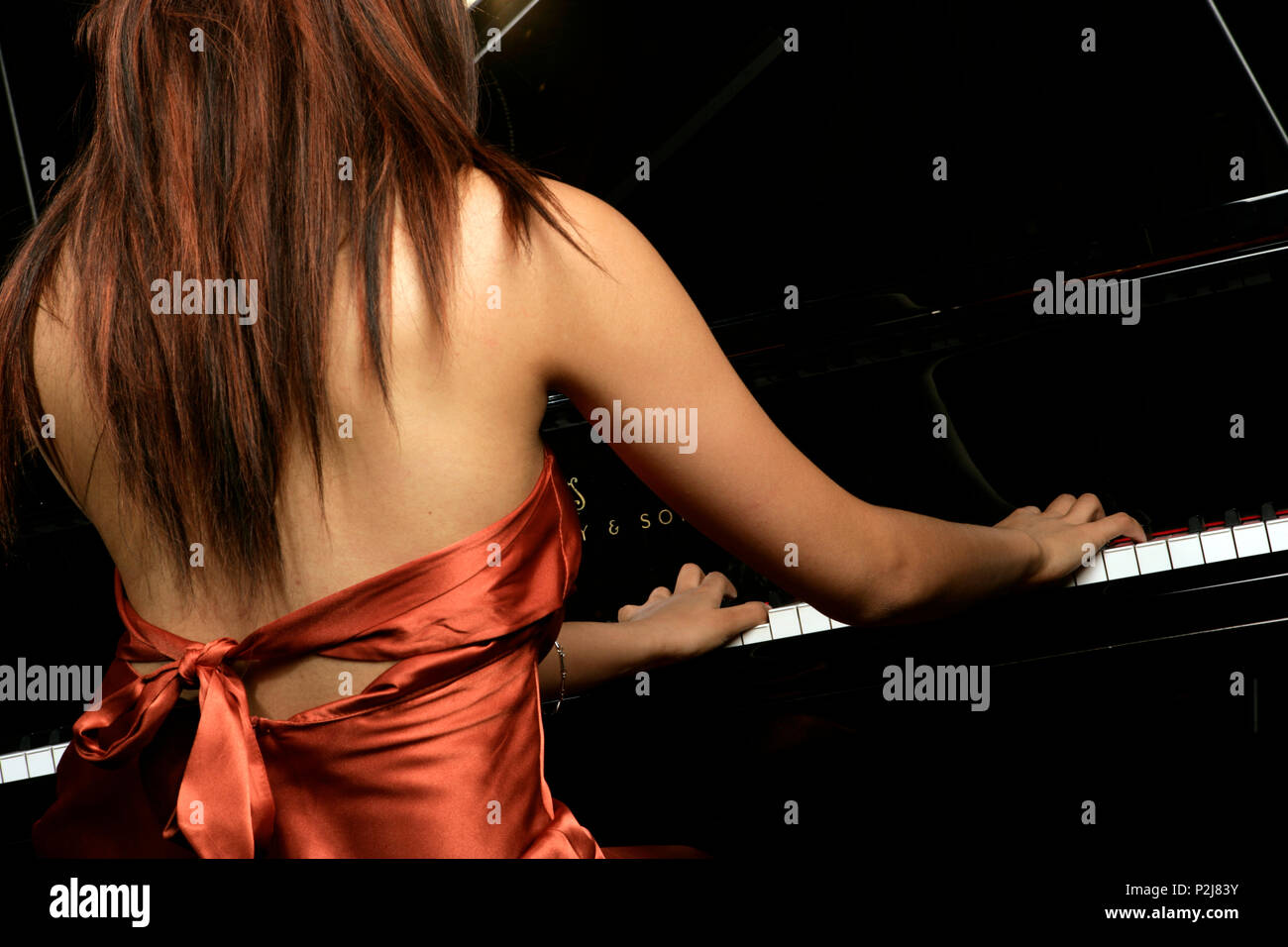 young woman playing the grand piano in a golden concert dress Stock Photo