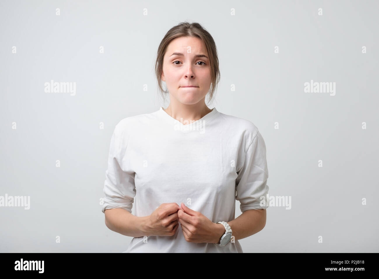 Portrait of beautiful girl in white t-shirt frowning her face in displeasure, keeping arms folded. Attractive young woman is angry and displeased Stock Photo