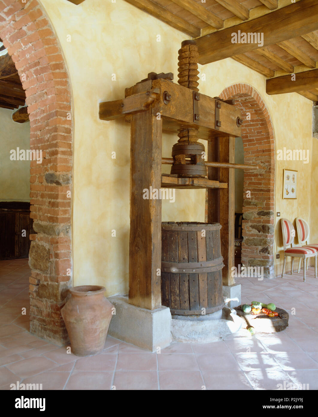 Large antique olive press and wooden barrel in Tuscan hall with tiled floor Stock Photo