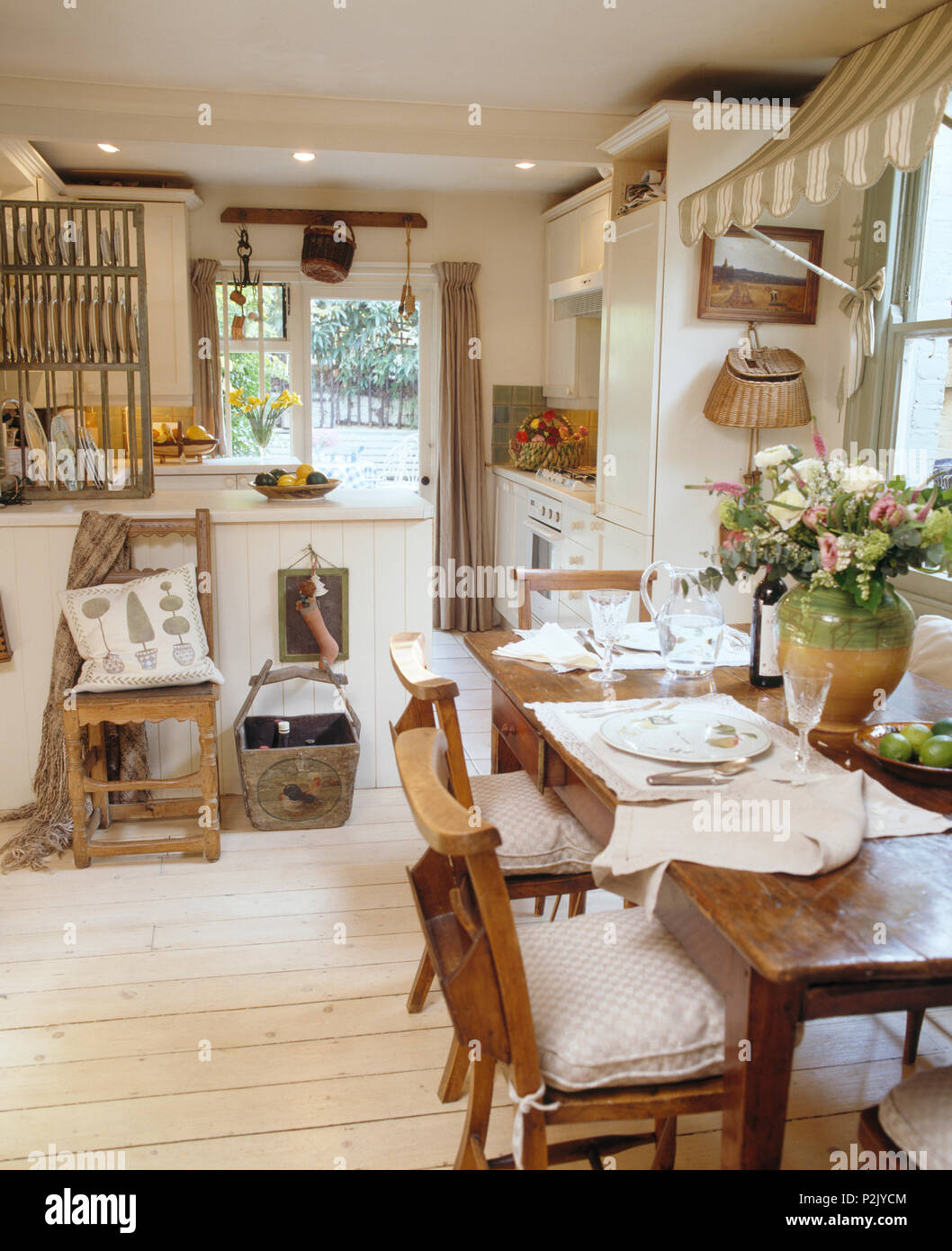 Old chapel chairs at simple wood table in country kitchen dining room with white painted floorboards Stock Photo