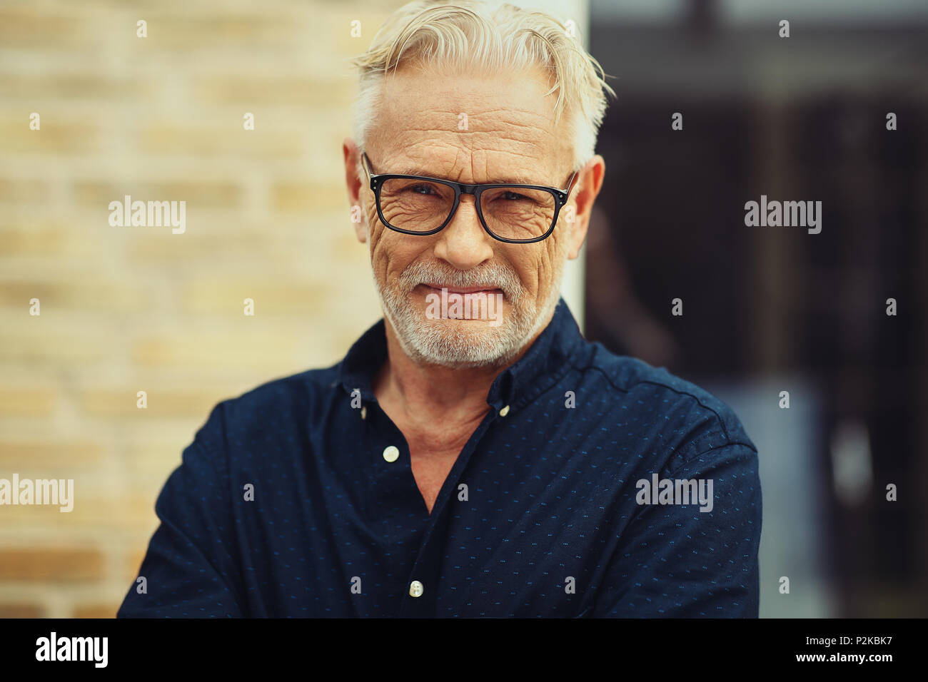 Smiling senior man with a beard and wearing glasses standing by himself outside in front of his home Stock Photo