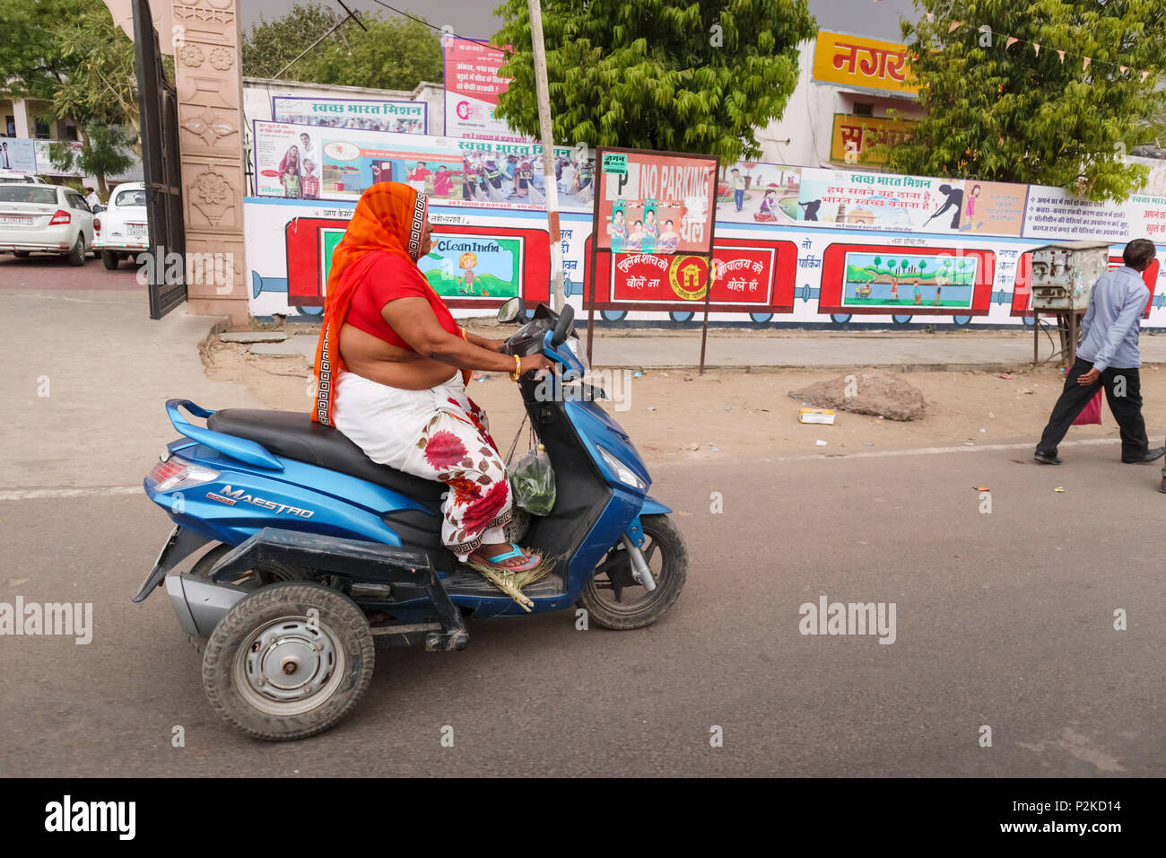Fat obese senior local woman wearing typical traditional local clothing riding a three wheeled motorcycle in the street in Dausa, Rajasthan, India Stock Photo