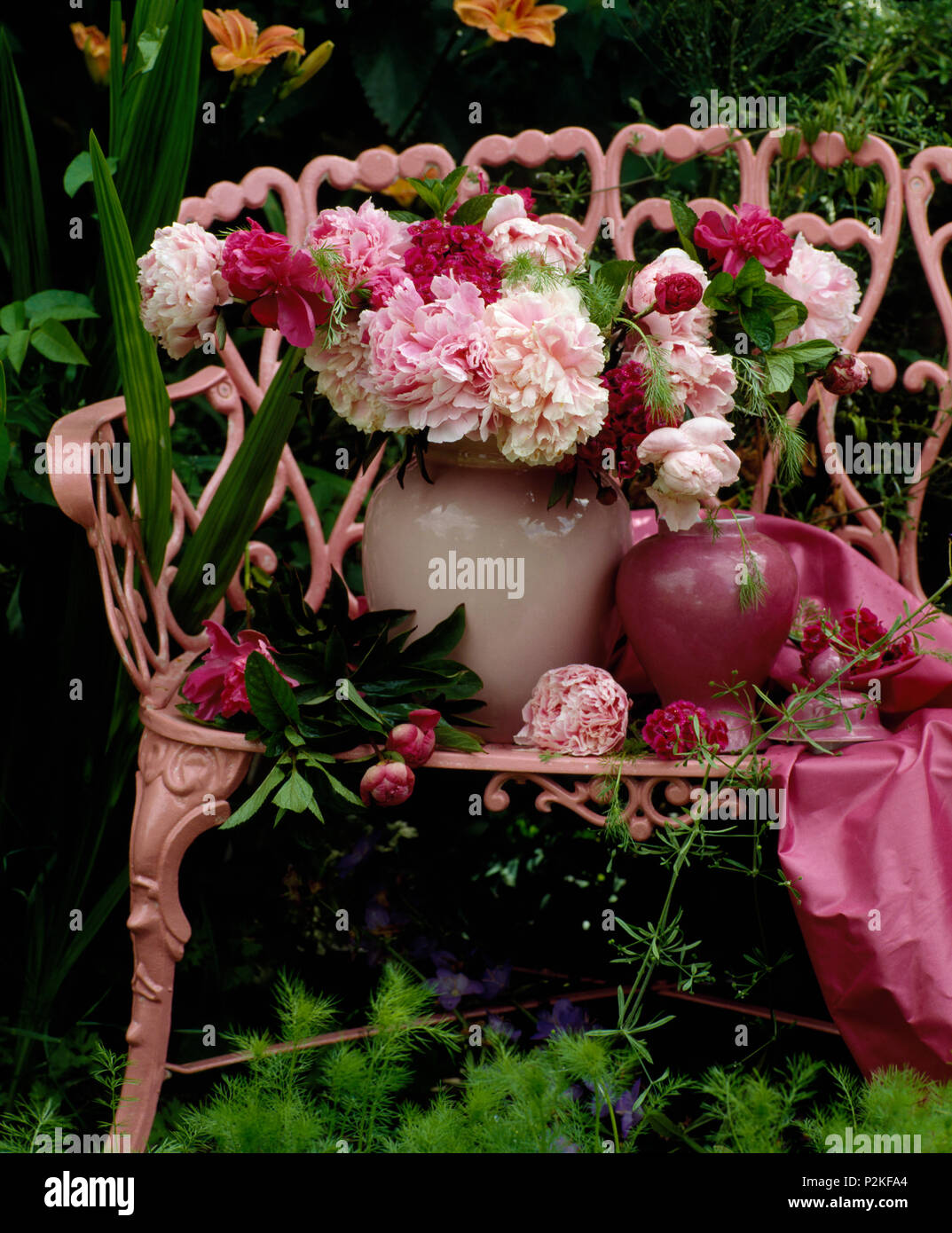 Still-Life of vase of pink peonies on pink painted garden bench Stock Photo