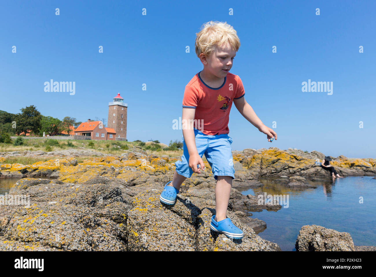 boy jumping from rock to rock along the shore near Hullehavn Camping, lighthouse, Summer, Baltic sea, MR, Bornholm, Svaneke, Den Stock Photo