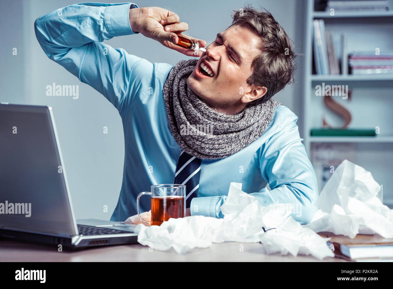 Sick employee using spray for nose. Photo of young man in office suffering virus of flu. Medical concept. Stock Photo