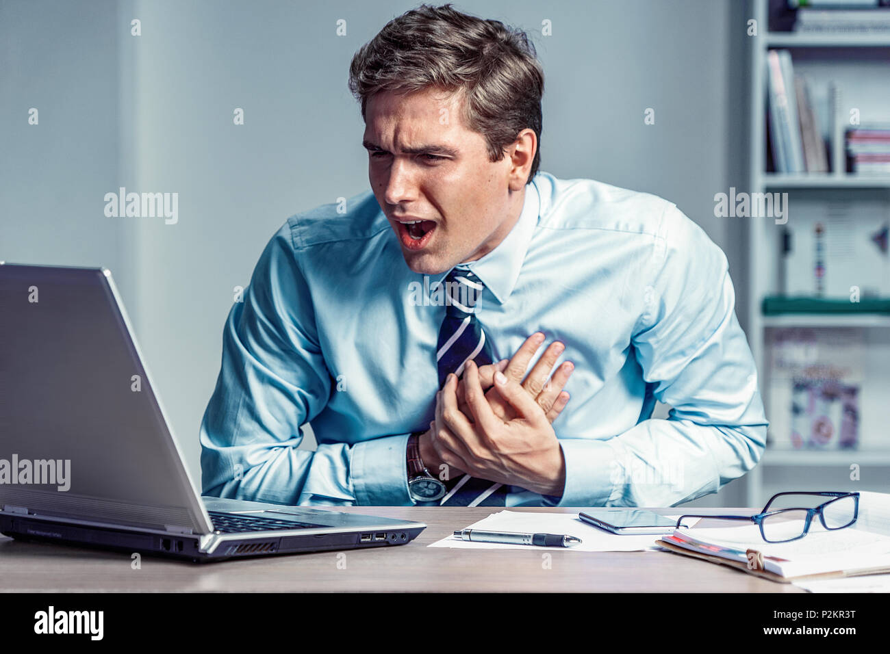Office manager having heart attack. Photo of young man holding hand on painful chest in the workplace. Medical concept. Stock Photo