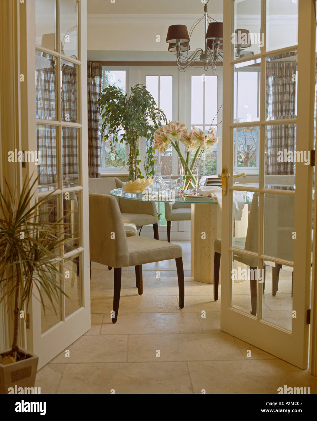 Glazed double doors open to modern dining room with cream upholstered chairs at glass table Stock Photo