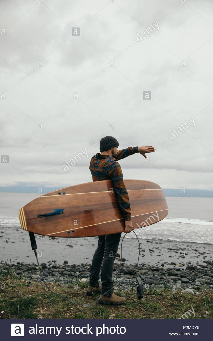 Male surfer with surfboard watching rugged ocean in anticipation Stock Photo