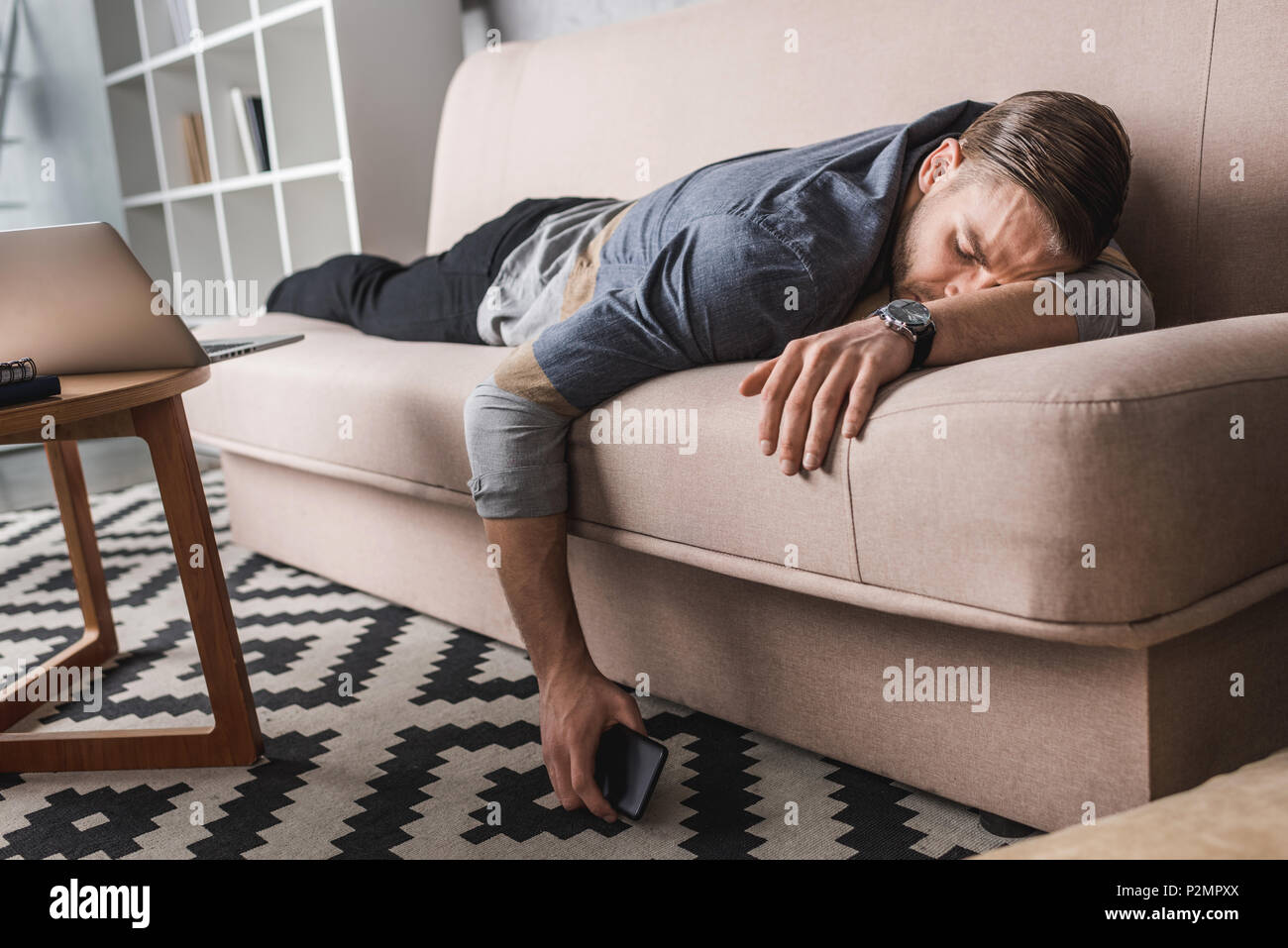 exhausted young man sleeping on couch with smartphone in hand Stock