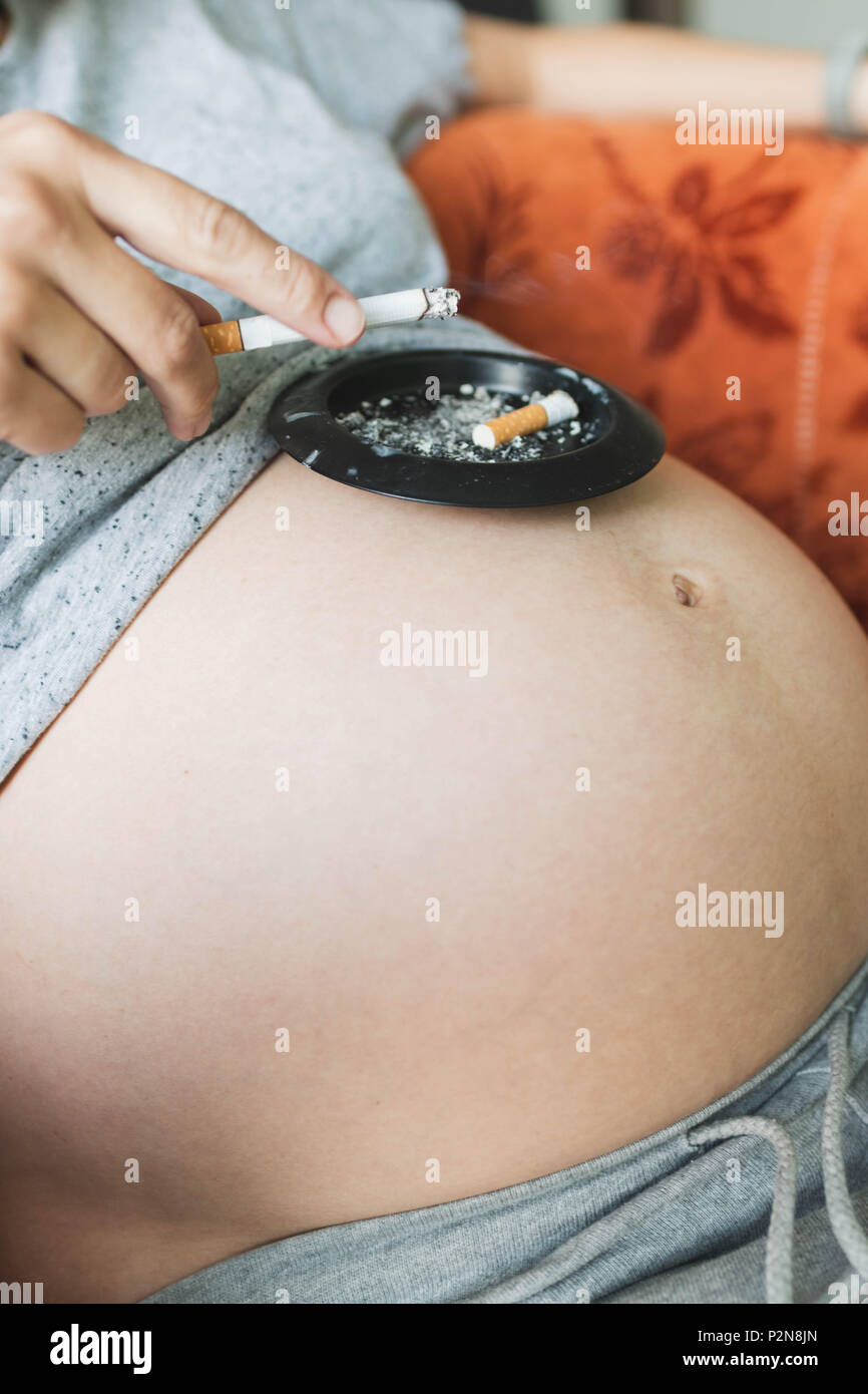 Anonymous pregnant woman smokes a cigarette, put the ashtray on the stomach  Stock Photo