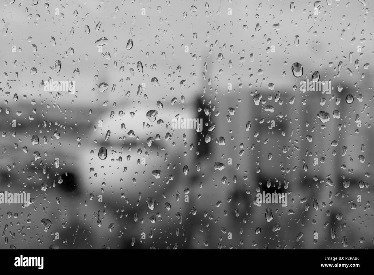 The outline of an airplane viewed from the window of an airport on a rainy day, selective focus on the drops of the water on the window - black and wh Stock Photo