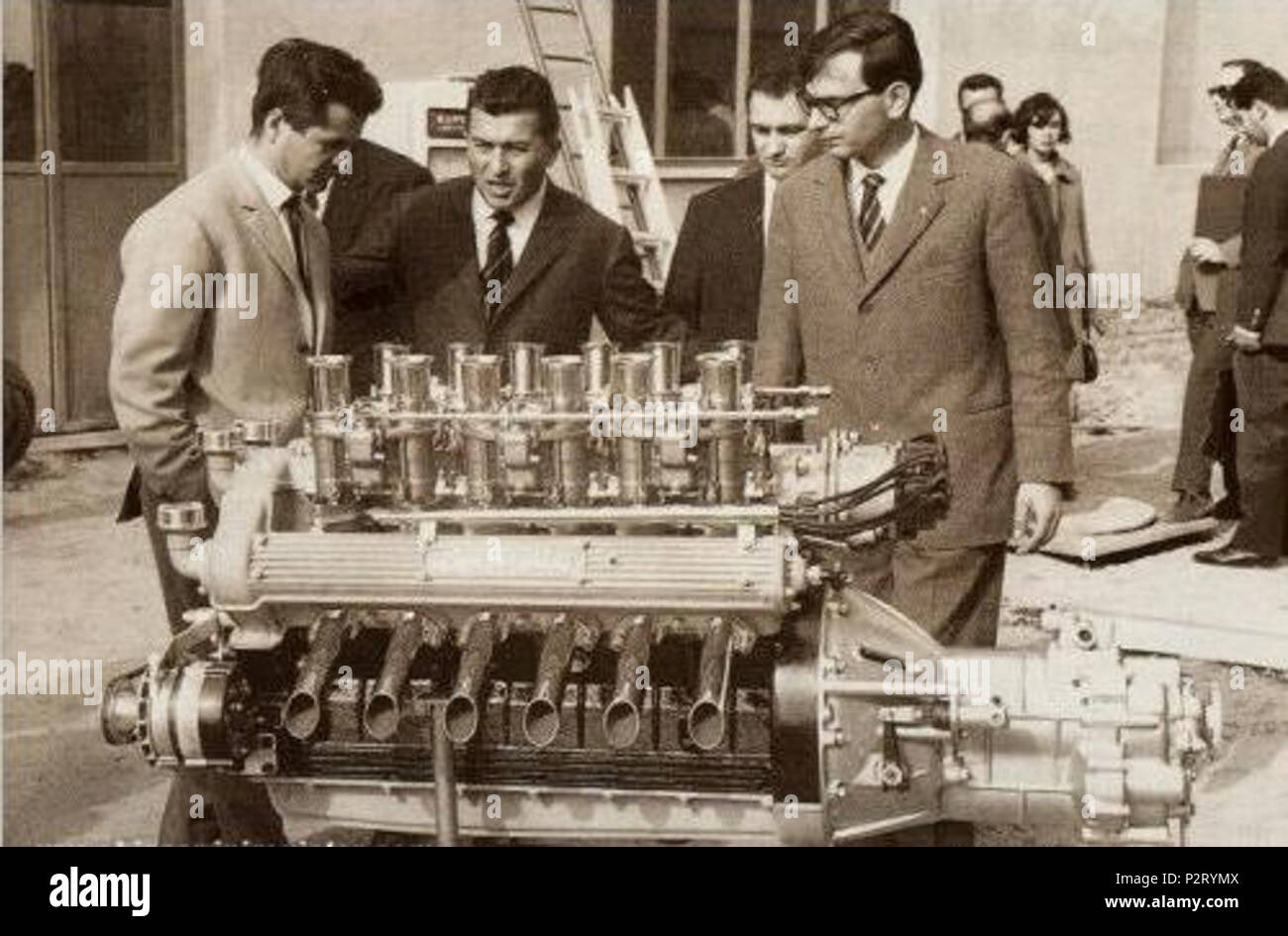 . English: From left to right: Giotto Bizzarrini, Ferruccio Lamborghini and Gian Paolo Dallara at Sant'Agata Bolognese in 1963, with a Lamborghini V12 engine prototype. Italiano: Da sinistra a destra: Giotto Bizzarrini, Ferruccio Lamborghini e Gian Paolo Dallara a Sant'Agata Bolognese, 1963, con un prototipo di motore Lamborghini V12. 1963. unknown; original it. uploader: Maxperot; Commons uploader: Khruner 11 Bizzarrini Lamborghini Dallara Stock Photo