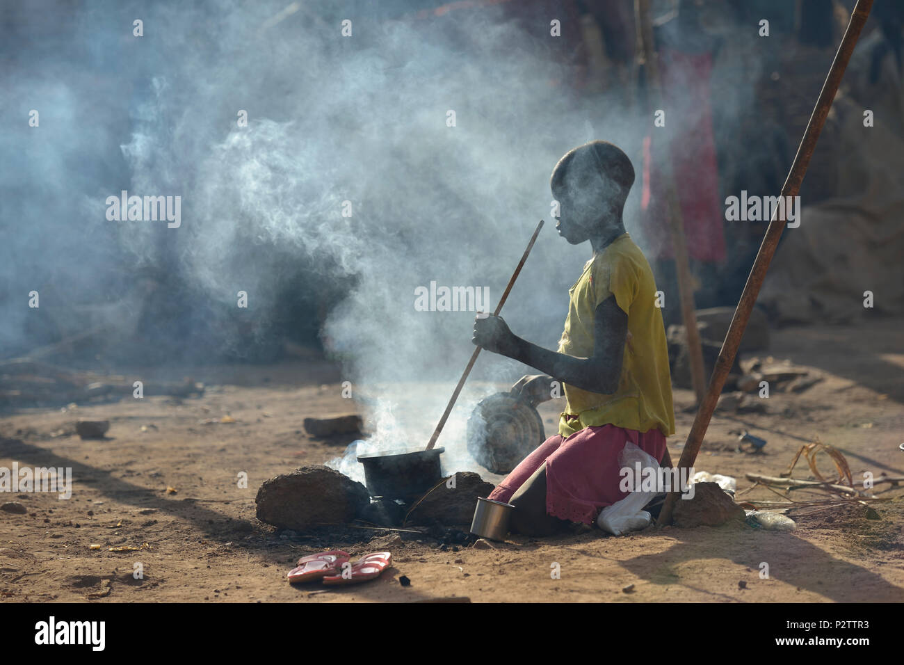 8-year old Adieu Anai cooks over a fire in a camp for more than 5,000 internally displaced persons in an Episcopal Church compound in Wau, South Sudan. Stock Photo