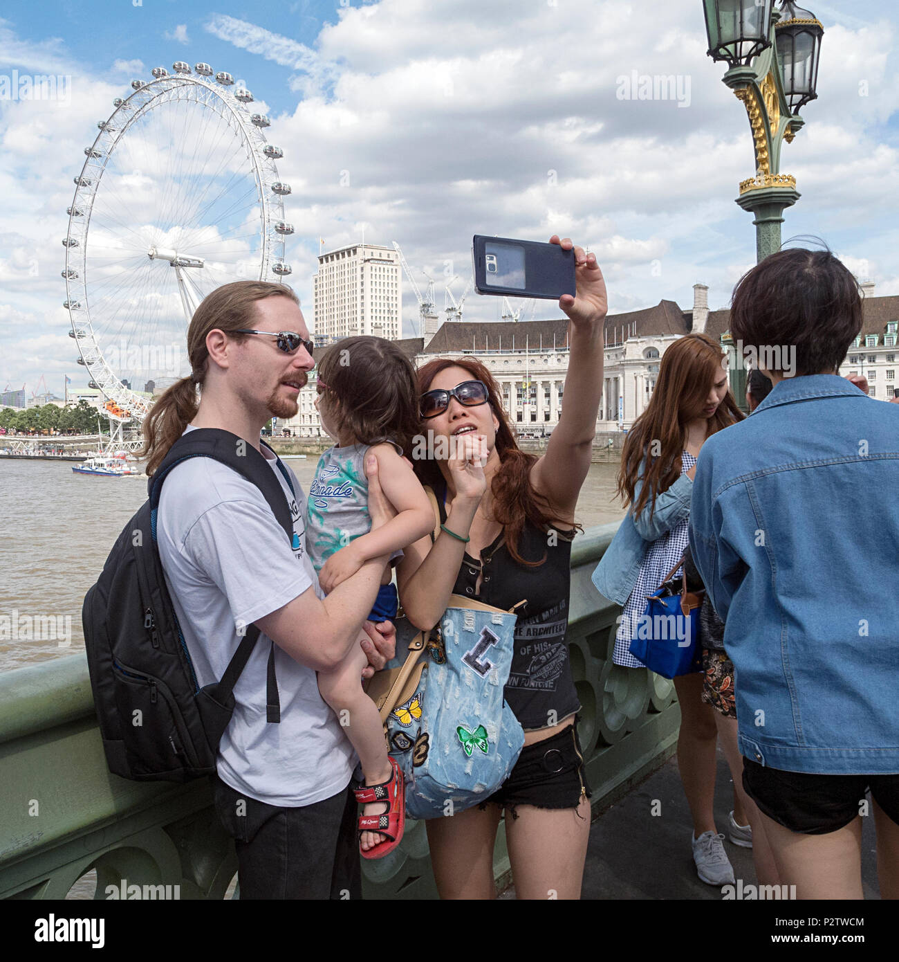 London, UK: July 25, 2016: Tourists take a photograph on Westminster Bridge with a view of Thames River behind them. Stock Photo