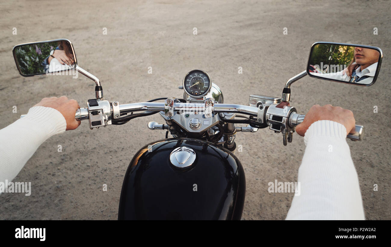 Guy's hands hold motorcycle control knobs closeup. In rearview mirror