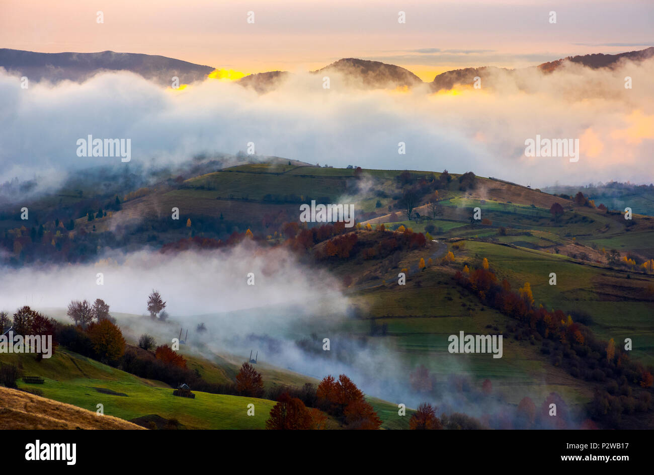 cloud inversion in autumn mountains at dawn. beautiful nature scenery. fog rolling above the rural fields Stock Photo