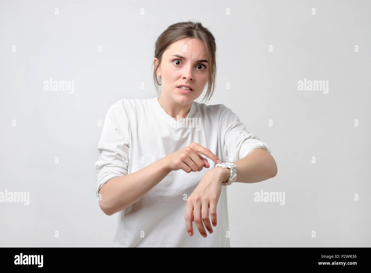 Young pretty caucasian student is angry because of being late. She is showing time on her watch. Concept of irritation of dead line. Stock Photo