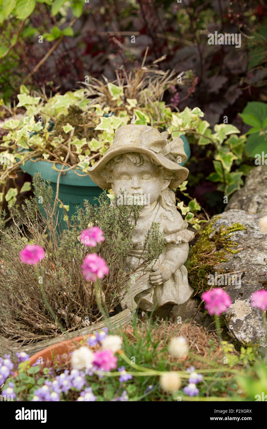A stone figurine of a boy set near a garden pond next to a pot of thyme. Lancashire North West England UK GB Stock Photo