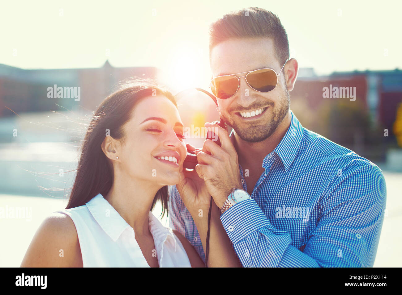 Young romantic caucasian couple sharing headphones outdoor in city, listening music in sunset Stock Photo