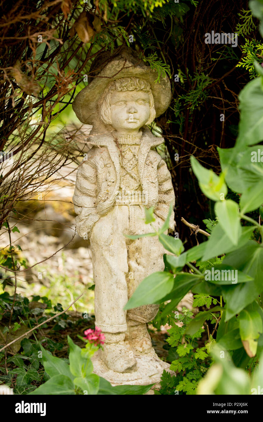 A stone figurine of a boy set near a garden pond. Lancashire North West England UK GB Stock Photo