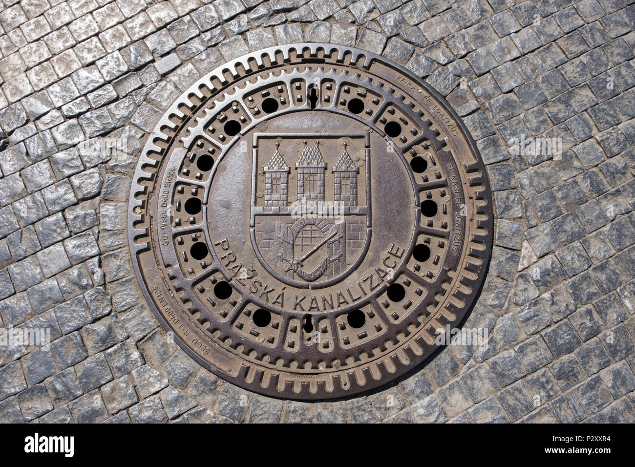 A manhole cover on a cobblestone street in the historic center of Prague, Czech Republic. The inscription means Prague's sewerage. Stock Photo