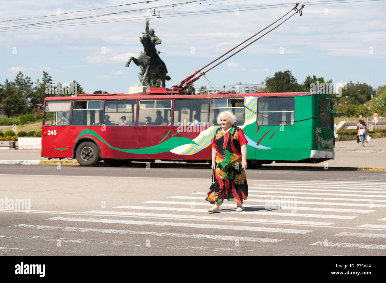 25.08.2016, Tiraspol, Transnistria, Moldova - Trolleybus in transnistrian colors, older lady in color matching dress crosses zebras on the central mai Stock Photo