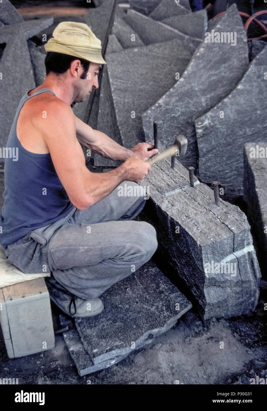 A professional stonecutter hammers a set of chisels into a crack in a block  of granite to separate a slab of the stone at a quarry in Riveo, a town in  the