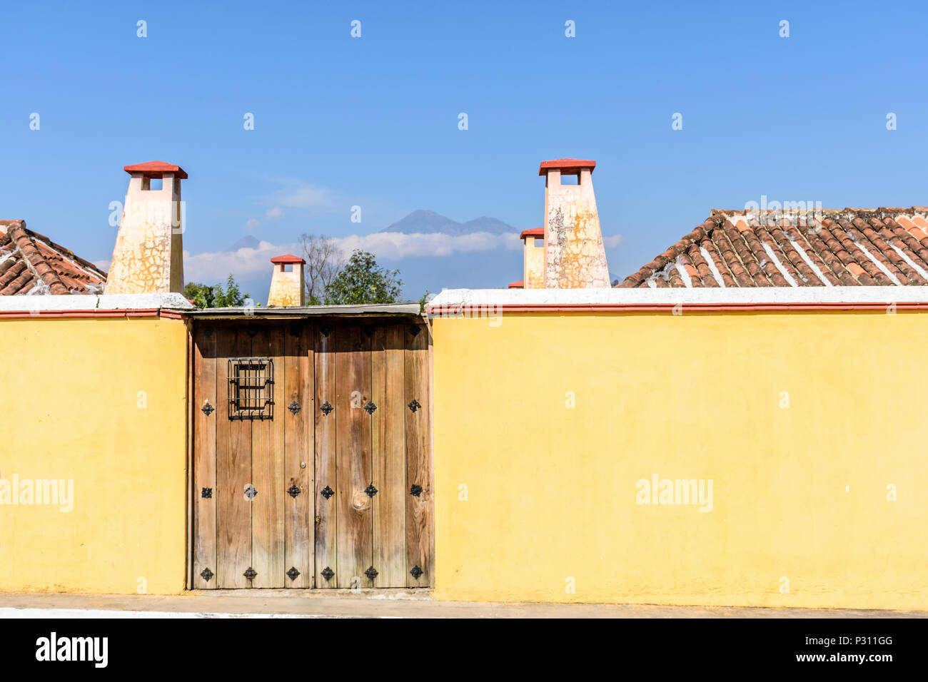 Yellow wall & gateway with volcanoes Fuego & Acatenango in distance in colonial city & UNESCO World Heritage Site of Antigua, Guatemala Stock Photo