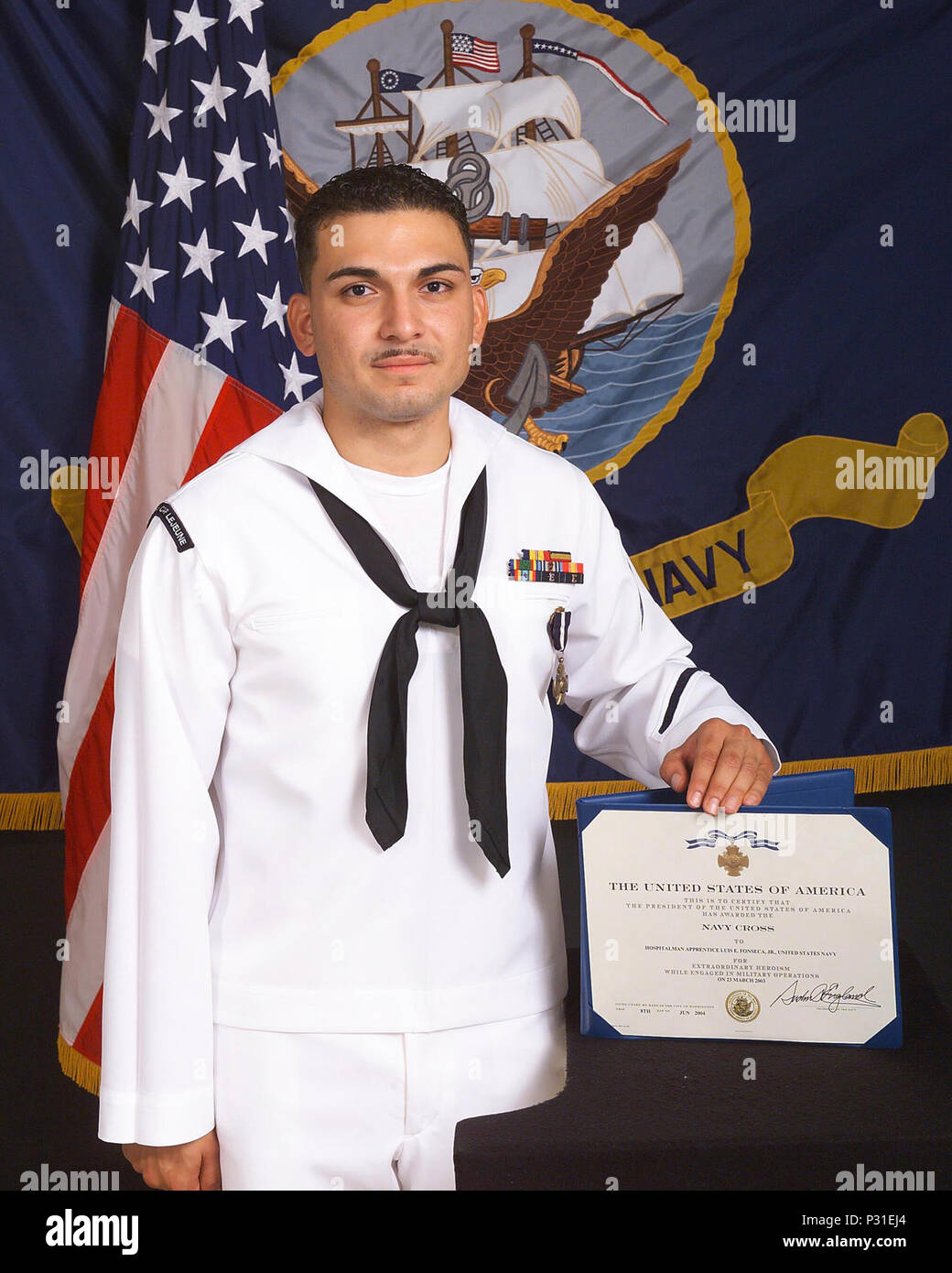 Lejeune, N.C. (Aug. 11, 2004) – Hospitalman Apprentice Luis E. Fonseca, Jr., stands with his Navy Cross citation that was presented to him by the Secretary of the Navy Gordon R. England, for heroism during the battle of An Nasiriyah, Iraq, in March 2003. Under attack and without concern of his own safety, Hospitalman Apprentice Fonseca braved small arms, machine gun, and intense rocket-propelled grenade fire to evacuate wounded Marines from a burning amphibious assault vehicle. He stabilized two casualties with lower limb amputations with tourniquets and administered morphine, while organizing Stock Photo