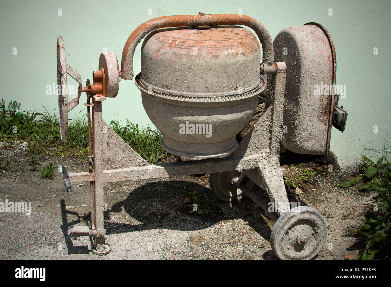 Dirty mini cement mixer in the the ground with little rocks and stones ,  tall green grasses behind it. Newly used equipment to build, fix structure  pu Stock Photo - Alamy