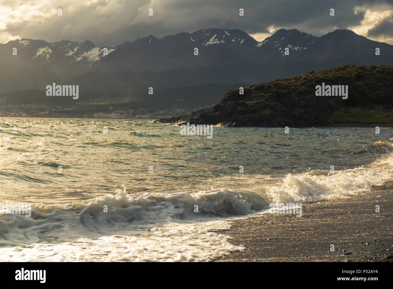 A wave ends on the beach of Playa Larga. In the background you see the fast-growing, touristic city of Ushuaia. Stock Photo