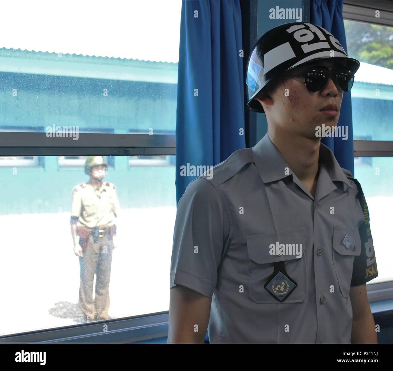 A South Korean Soldier stands guard inside the main conference building straddling North and South Korea Aug. 16, protecting the Soldiers of the 1st Armored Brigade Combat Team, 1st Cavalry Division, who were inside the building getting a firsthand look at where negotiations take place between the United Nations Command and North Korea. Outside the window, a North Korean Soldier stands guard. (U.S. Army photo by Spc. Jeremy Reuse, 2nd Battalion, 8th Cavalry Regiment, 1st Armored Brigade Combat Team, 1st Cav. Div.) Stock Photo
