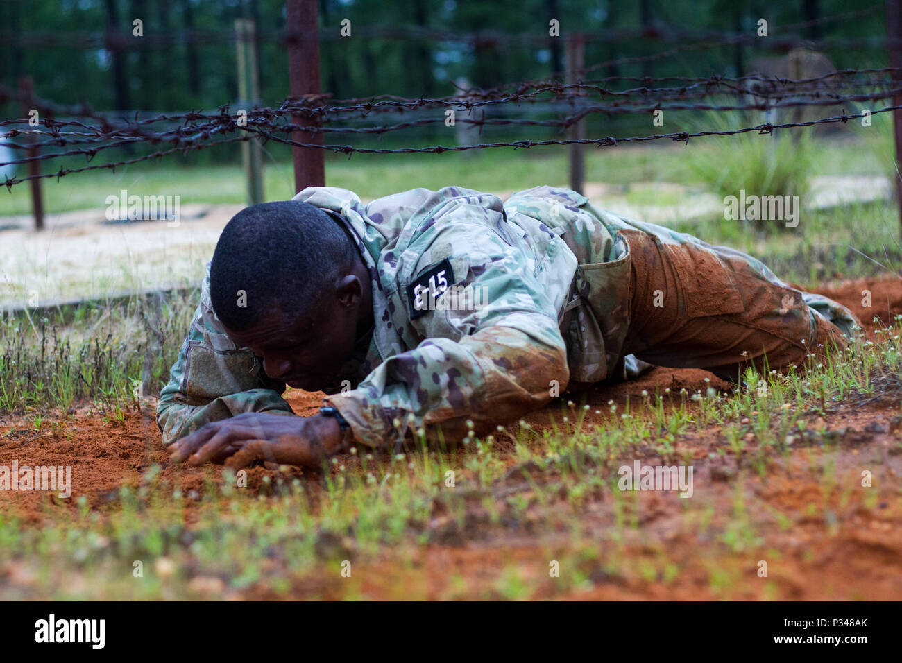 U.S. Army Spc. Pateh Jawo, a medical laboratory specialist from Bronx, New York, with the 7387th Blood Detachment, U.S. Army Reserve Medical Command, performs a low crawl on obstacle four of the Fort Bragg Air Assault School Obstacle Course. Touching the barbed wire with any part of their body during this lane results in disqualification, requiring the competitor to be returned to the beginning of the lane to try again or continue with a loss of points.  Thirty-six warriors continue to vie for the title of United States Army Reserve Best Warrior during the grueling multifaceted competition tha Stock Photo