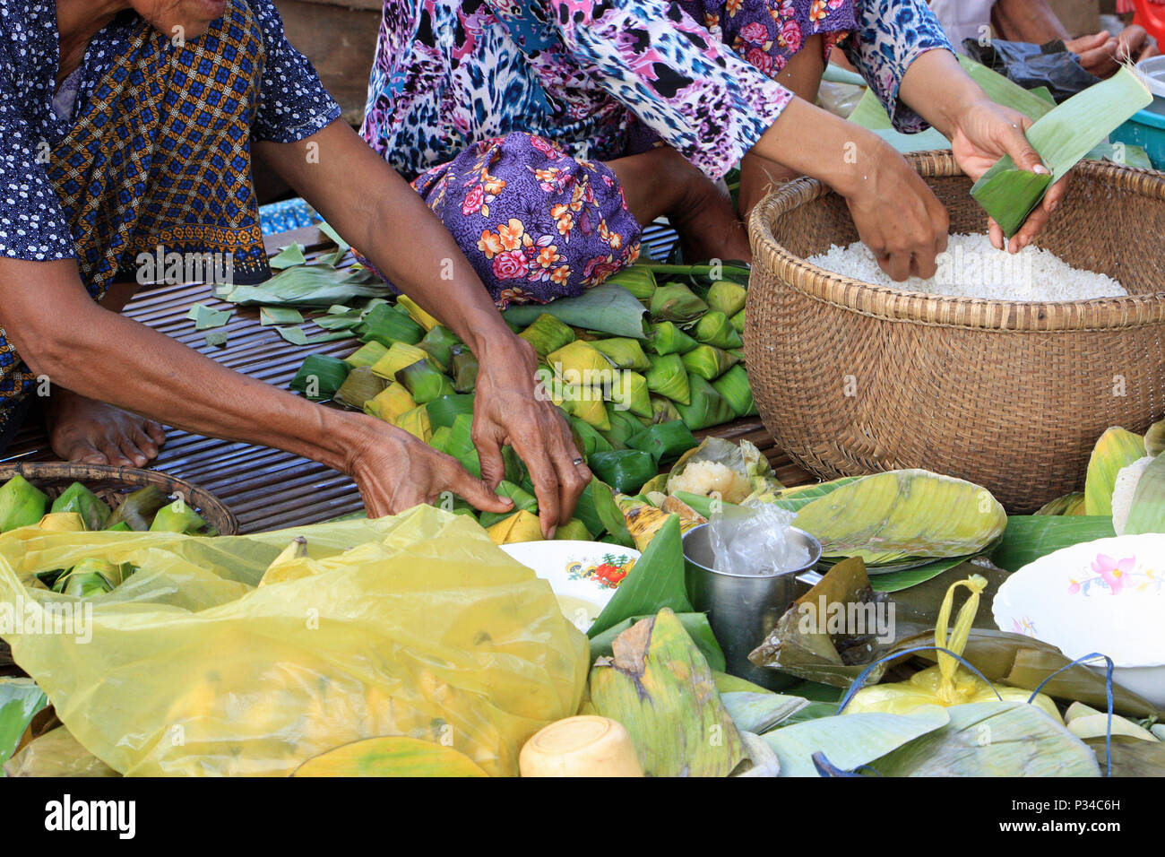 Preparing food for a wedding, wrapping rice and sweetmeats in banana leaves, ready for cooking on open fires outdoors. Stock Photo