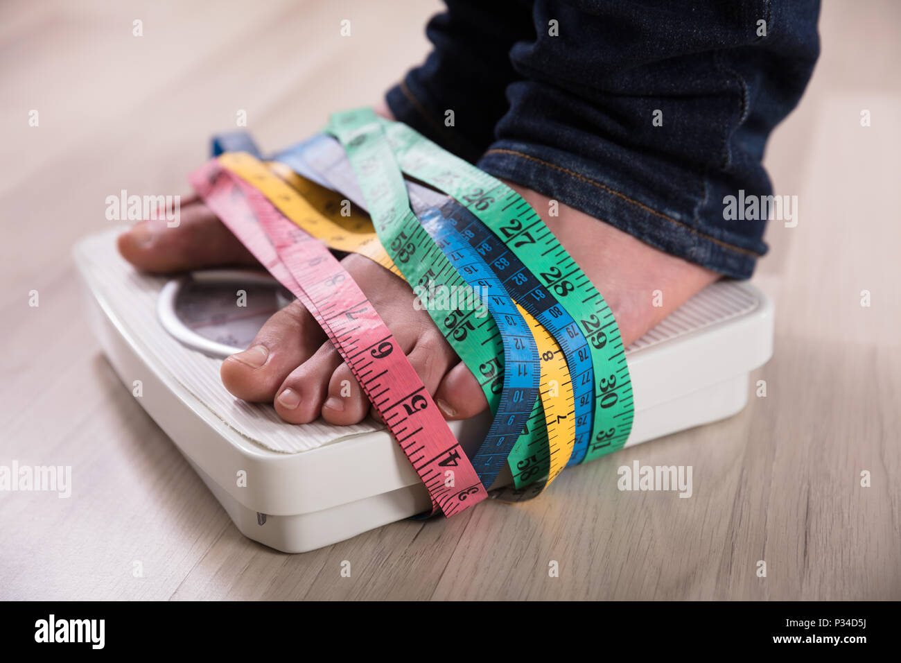 https://c8.alamy.com/comp/P34D5J/close-up-of-a-persons-feet-on-weight-scale-wrapped-with-multi-colored-measuring-tape-P34D5J.jpg