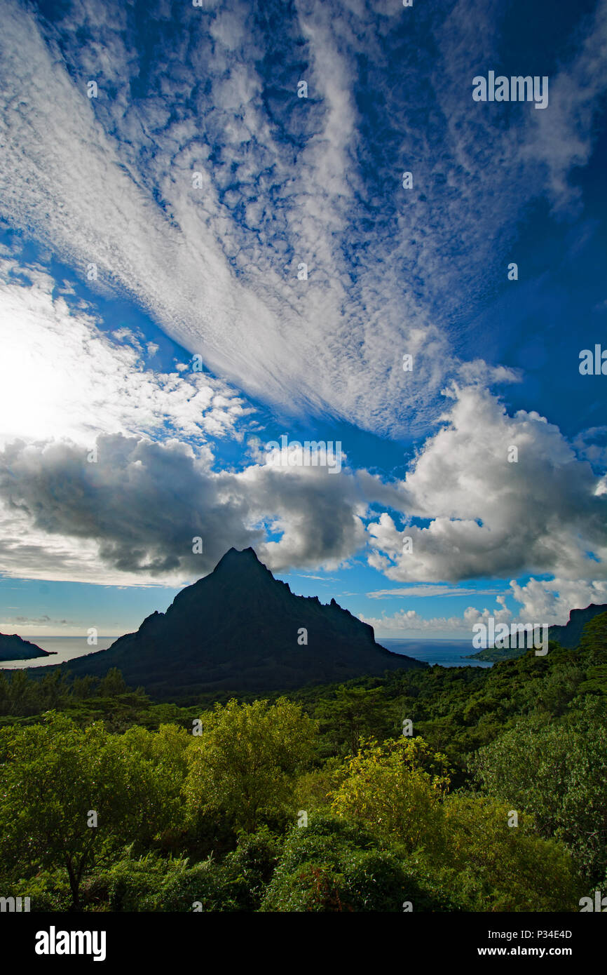 Mountain peak  in the jungle covered hills of Moorea with a backdrop of spectacular clouds against a blue sky. Stock Photo