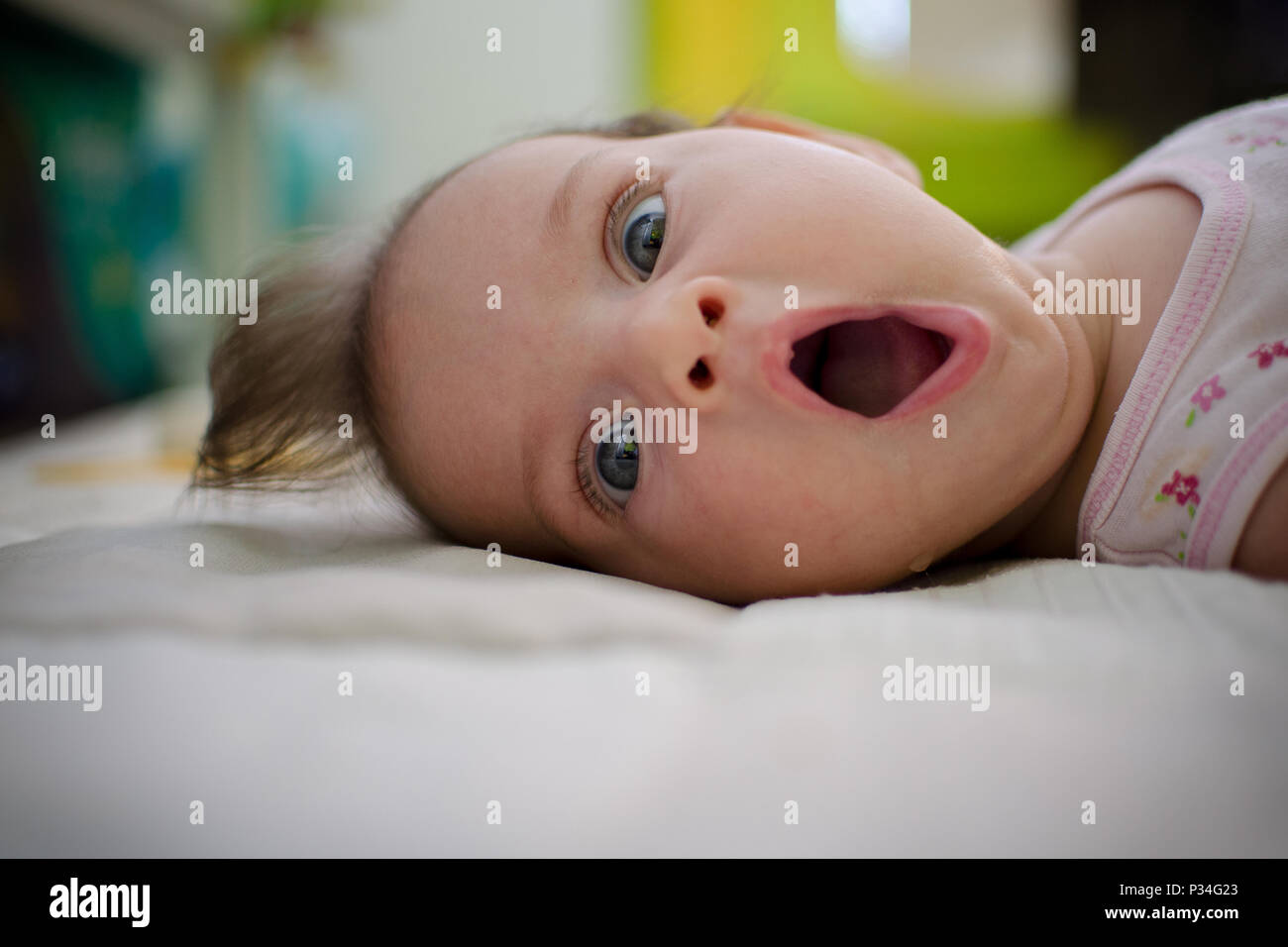 Portrait of a baby laying on the bed with a surprised expression of utter consternation on her face. Stock Photo