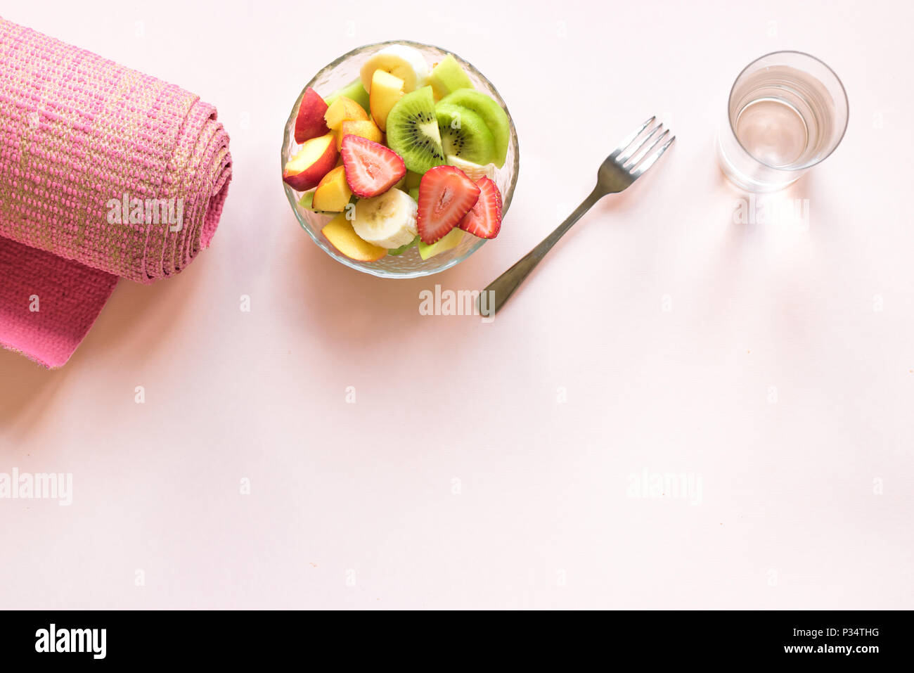 Sport and healthy lifestyle concept. Pink yoga mat and Fruit and Berries Salad in bowl for snack or breakfast on pink pastel background, copy space. Stock Photo