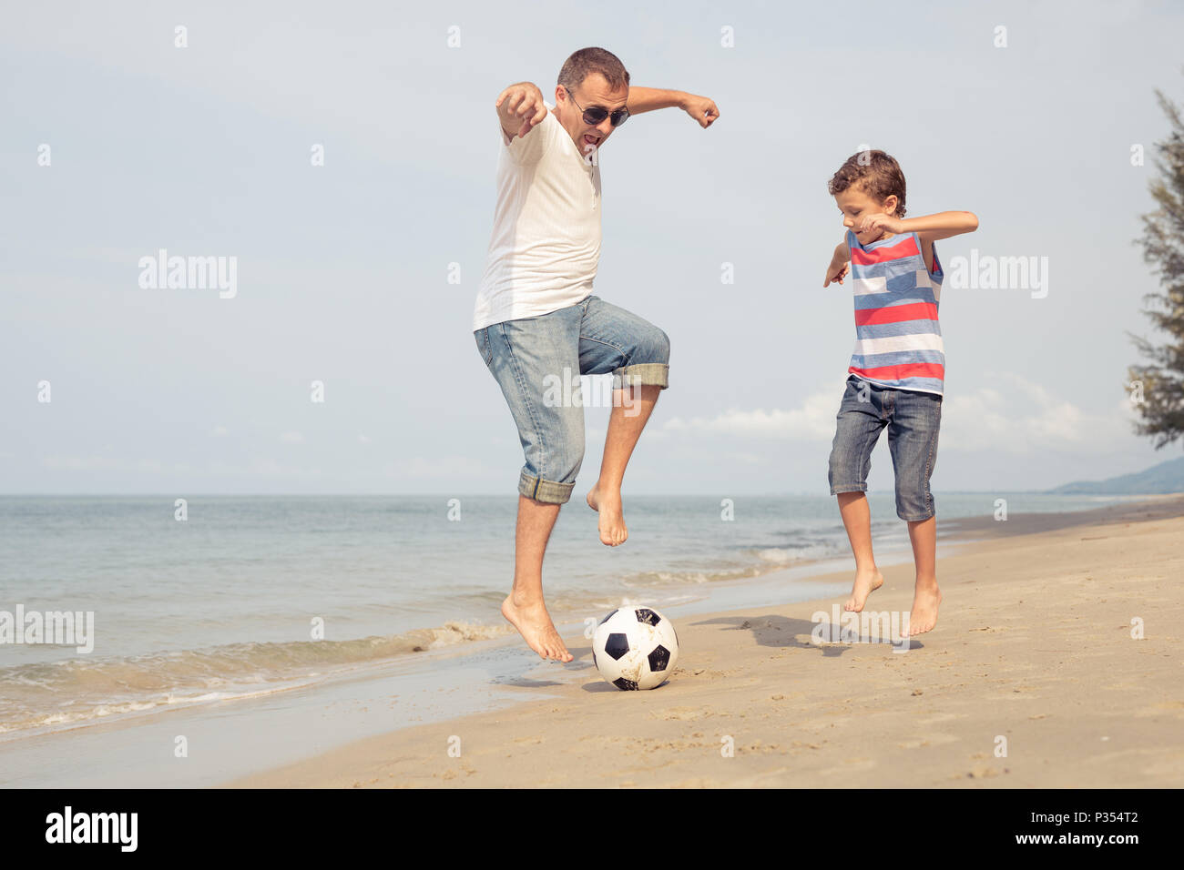 Father and son playing football on the beach at the summer day time. People having fun outdoors. Concept of friendly family. Stock Photo