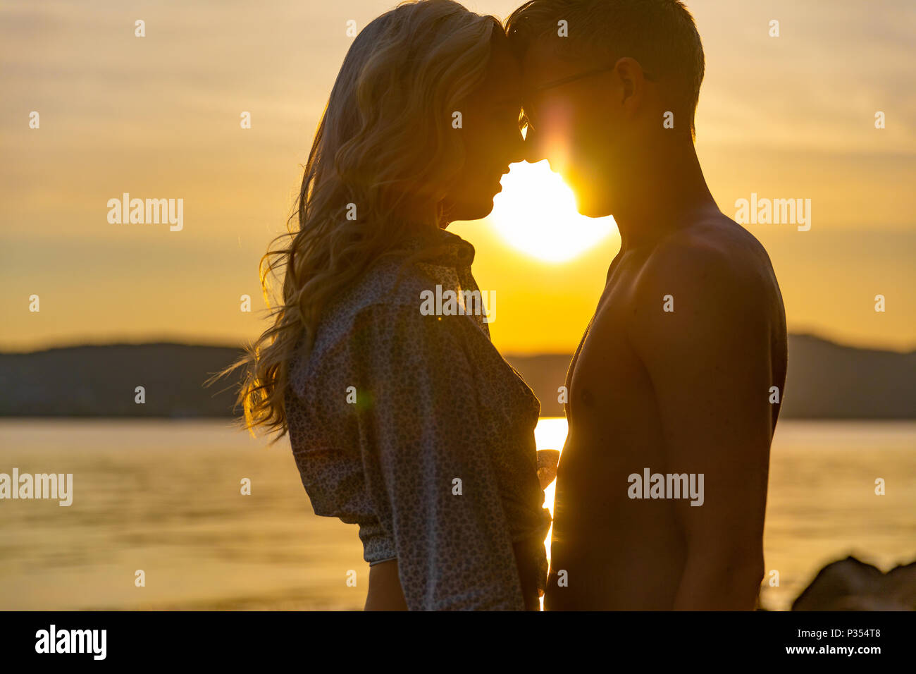 Silhouette of couple in love embracing at the beach against sun Stock Photo